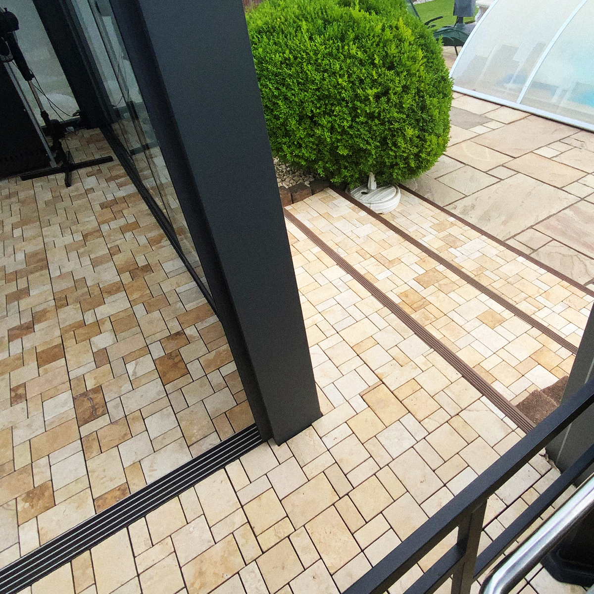 Travertin Klickfliesen in warmem Beige auf einer überdachten Terrasse mit Übergang zum Wintergarten